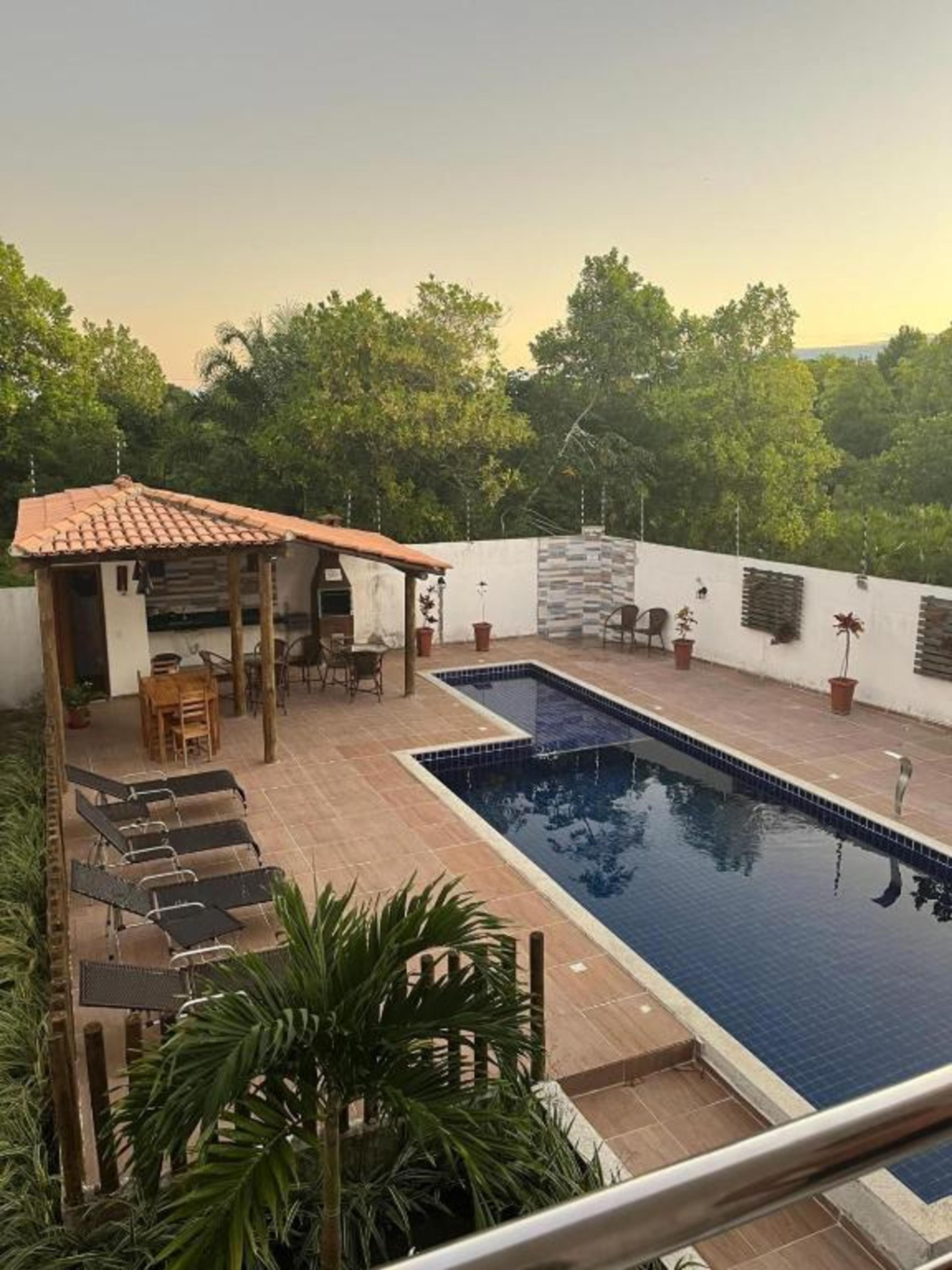 A swimming pool with a tiled deck, a covered seating area, and potted plants.