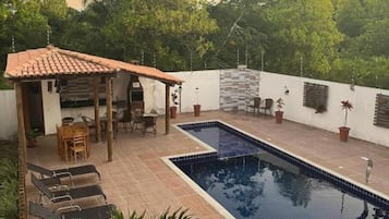 Piscina com deck azulejado, área de estar coberta e vasos de plantas.