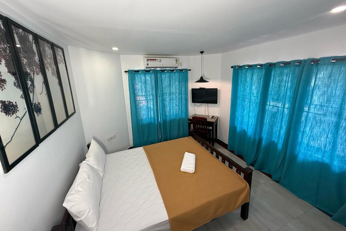 Una habitación de hotel con una cama, un escritorio, una silla, un televisor y cortinas.