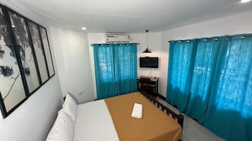 A hotel room with a bed, a desk, a chair, a TV, and curtains.