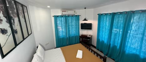 A hotel room with a bed, a desk, a chair, a TV, and curtains.