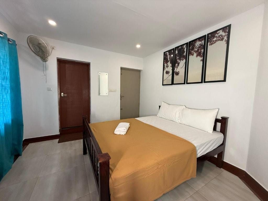 Quarto de hotel com uma cama, um ventilador, uma porta e uma obra de arte na parede.