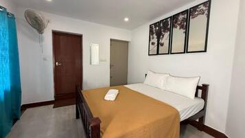 Quarto de hotel com uma cama, um ventilador, uma porta e uma obra de arte na parede.