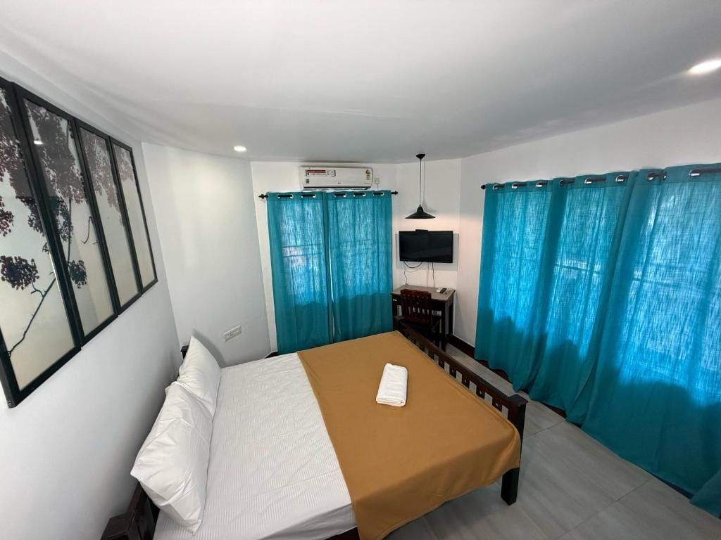 Una habitación de hotel con cama, televisión de pantalla plana, aire acondicionado y cortinas azules.