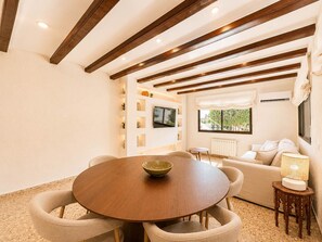 Ein Essbereich mit einem runden Tisch, Stühlen und einer Schüssel. Im Hintergrund befindet sich eine Couch und eine Lampe.