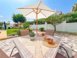 Eine Terrassenanlage mit Tisch, Stühlen, einem großen Sonnenschirm und Blumentöpfen.