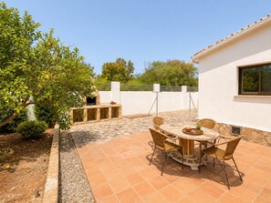 An outdoor patio with a stone-tiled floor, a round table with chairs, and a barbecue grill. - Villa Las Marinas CF with Private Pool near the Beach in Dénia (Denia)