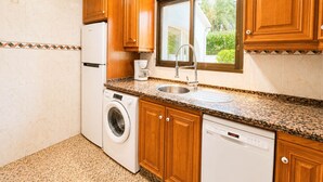 Een functionele keuken met houten kastjes, een ingebouwde wasmachine, een vaatwasser en een raam met uitzicht op groen.