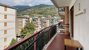 Un balcon donnant sur une ville perchée sur une colline, un pot de fleurs et un banc en bois.