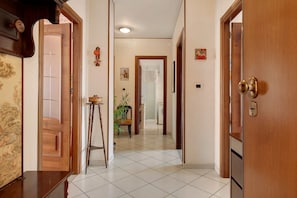 Un pasillo con una puerta de madera a la derecha, una mesita con una silla y una planta en el centro.