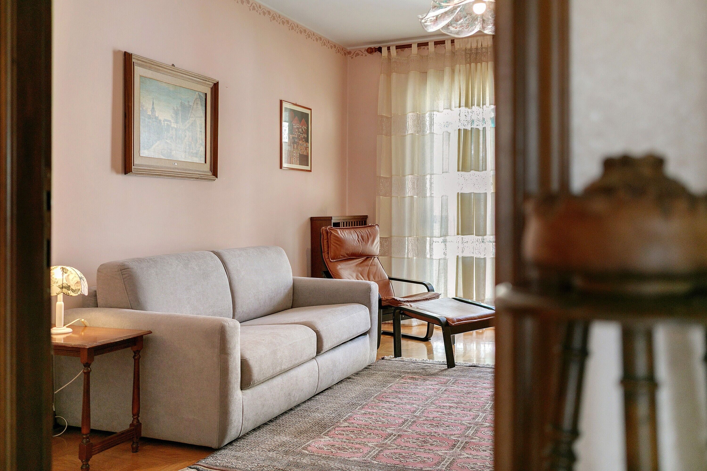 A living room with a sofa, a chair, a small table, and a rug. There are two framed pictures on the wall.