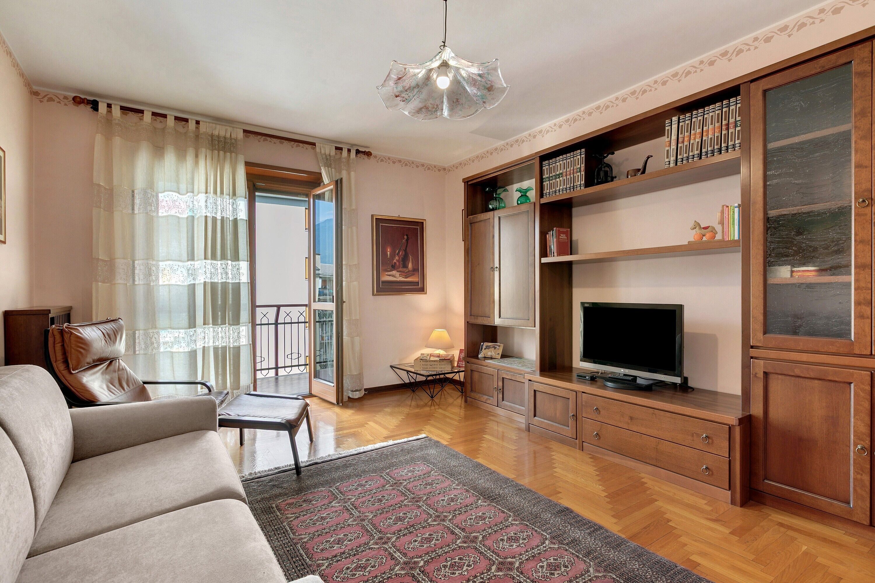A living room with a sofa, television, wooden cabinet, and a patterned rug.