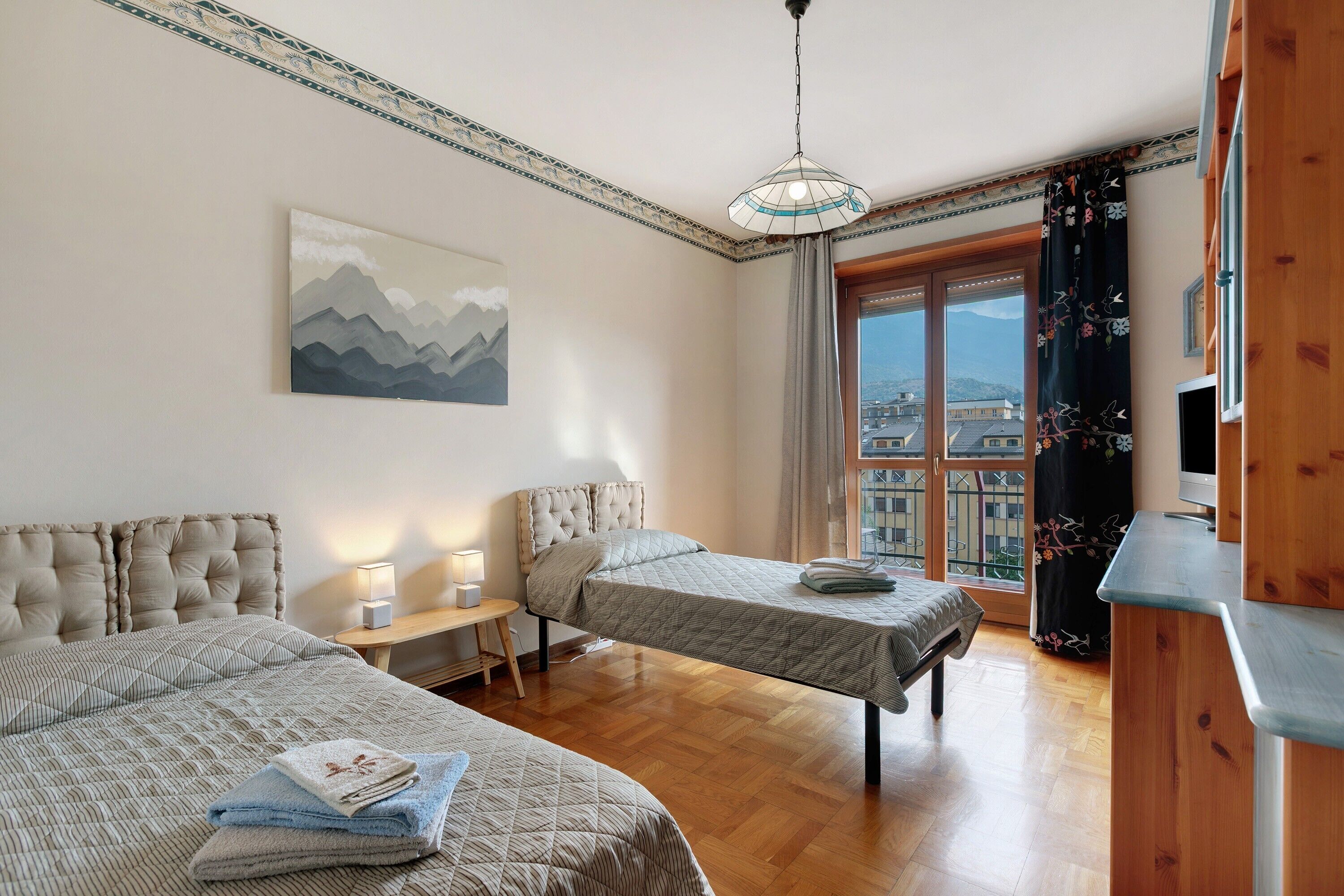 Una habitación de hotel con dos camas, un cuadro, una ventana con vistas y un armario de madera.