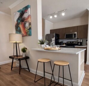 A modern kitchen with a central island, bar stools, a lamp, and a painting on the wall.