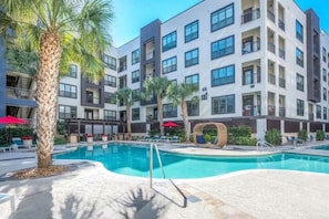 A modern building with a swimming pool, palm trees, and outdoor seating areas.