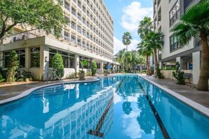 A swimming pool with clear water, surrounded by buildings and palm trees.