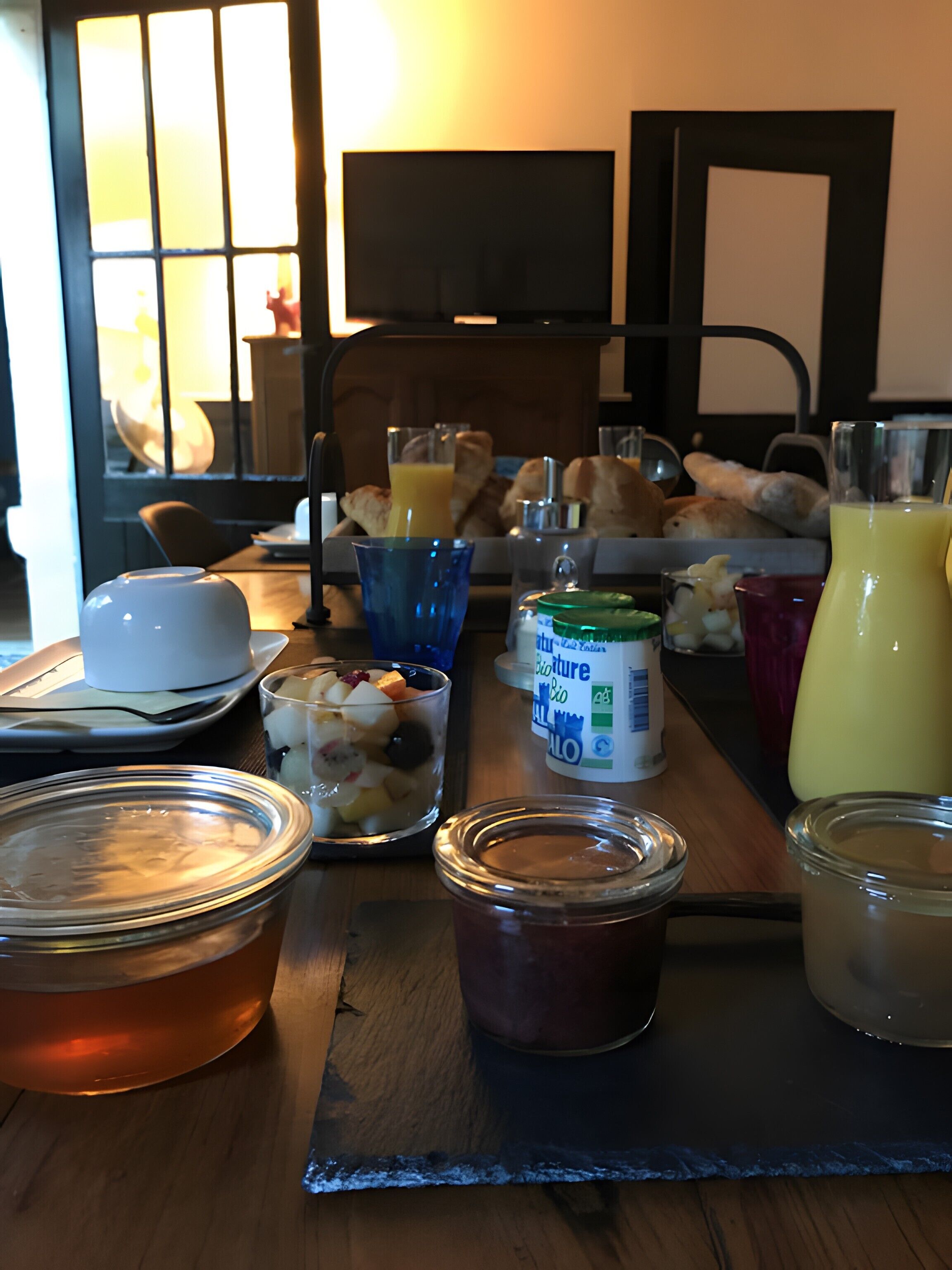 Une table de petit-déjeuner avec divers aliments et boissons, notamment un verre de jus d’orange, un pot de confiture et un verre de lait.
