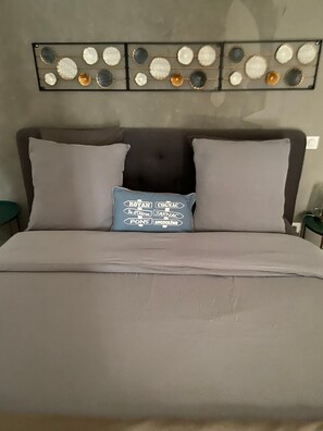 A bed with a grey headboard, two pillows, and a decorative wall piece above.