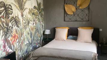 Une chambre avec une grande fresque murale, un lit avec de nombreux coussins, une table de chevet et un banc.