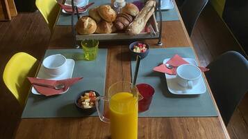 Ett matbord dukat med frukosttillbehör, inklusive bakverk, en kanna med apelsinjuice och en skål med frukt.