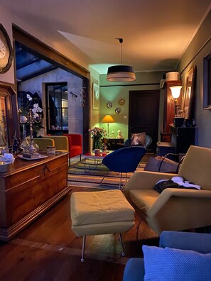 Ein Wohnzimmer mit einem Holzschrank, einem blauen Sessel, einem beigen Hocker und einem Sofa.