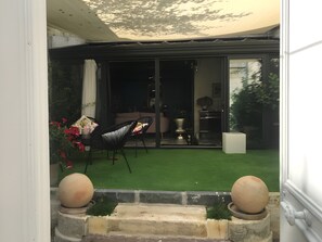 A patio with artificial grass, a dining table with chairs, and a sliding glass door leading to an interior space.