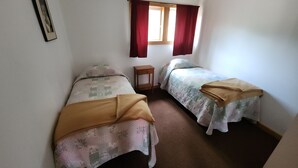 A small, single-room accommodation with two beds, a small table, and a window with curtains.