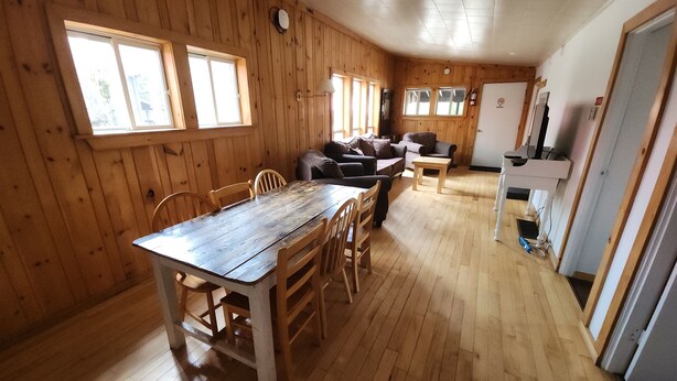 A wooden-paneled room with a dining table and chairs, a sofa, and a kitchenette area.