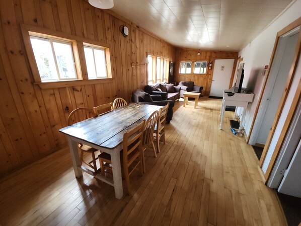Une pièce aux murs lambrissés, comprenant une table à manger et des chaises, un canapé et un coin cuisine.