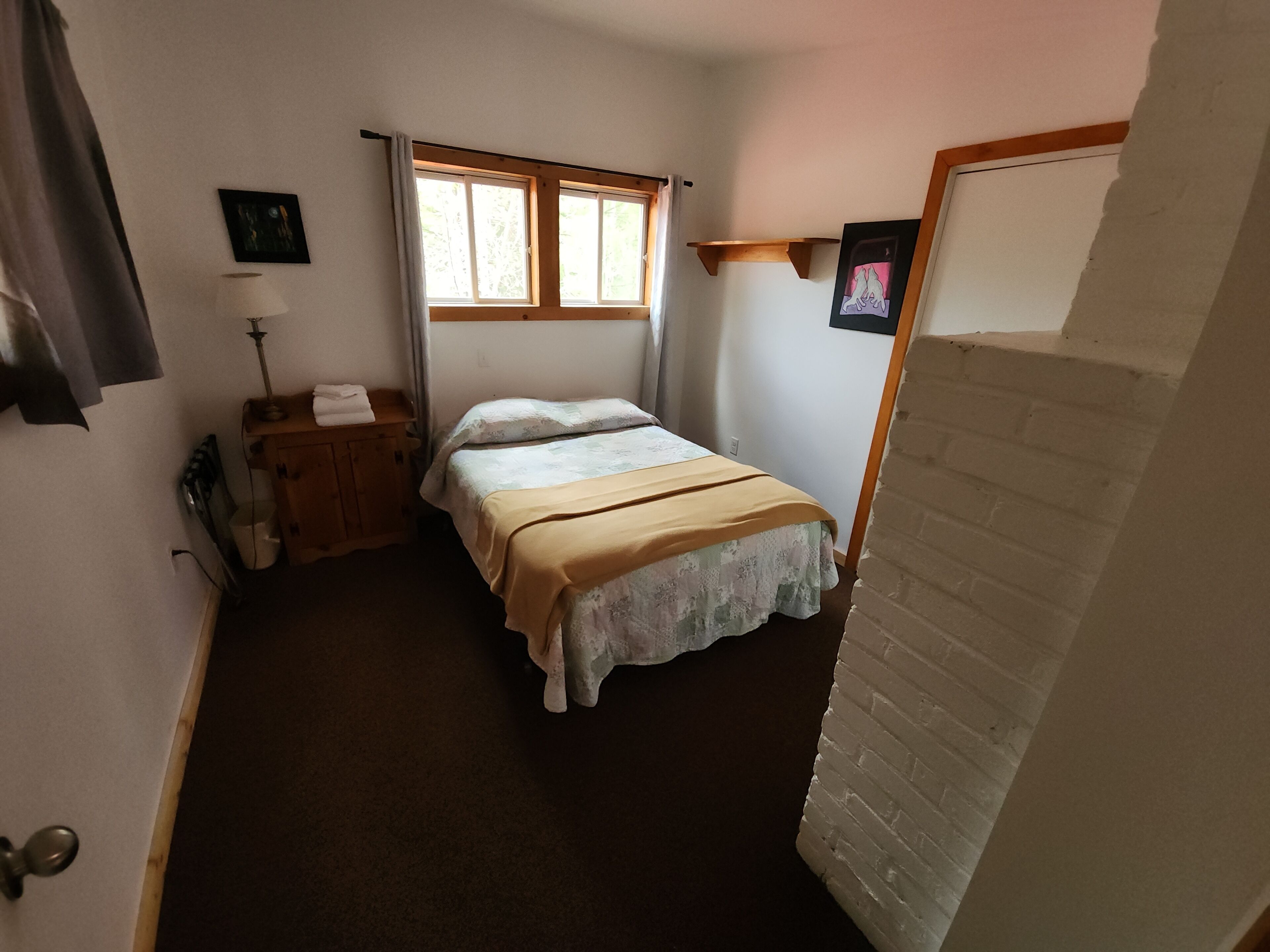 A bedroom with a bed, a nightstand, a lamp, and a window.