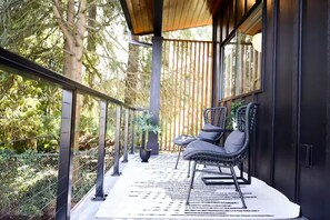 Een balkon met een stoel en tafel, omgeven door een houten hekwerk en glazen wanden, met uitzicht op een bebost gebied.