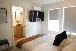 Een slaapkamer met een bed, een aan de muur bevestigde televisie, een raam en een deur naar een badkamer.