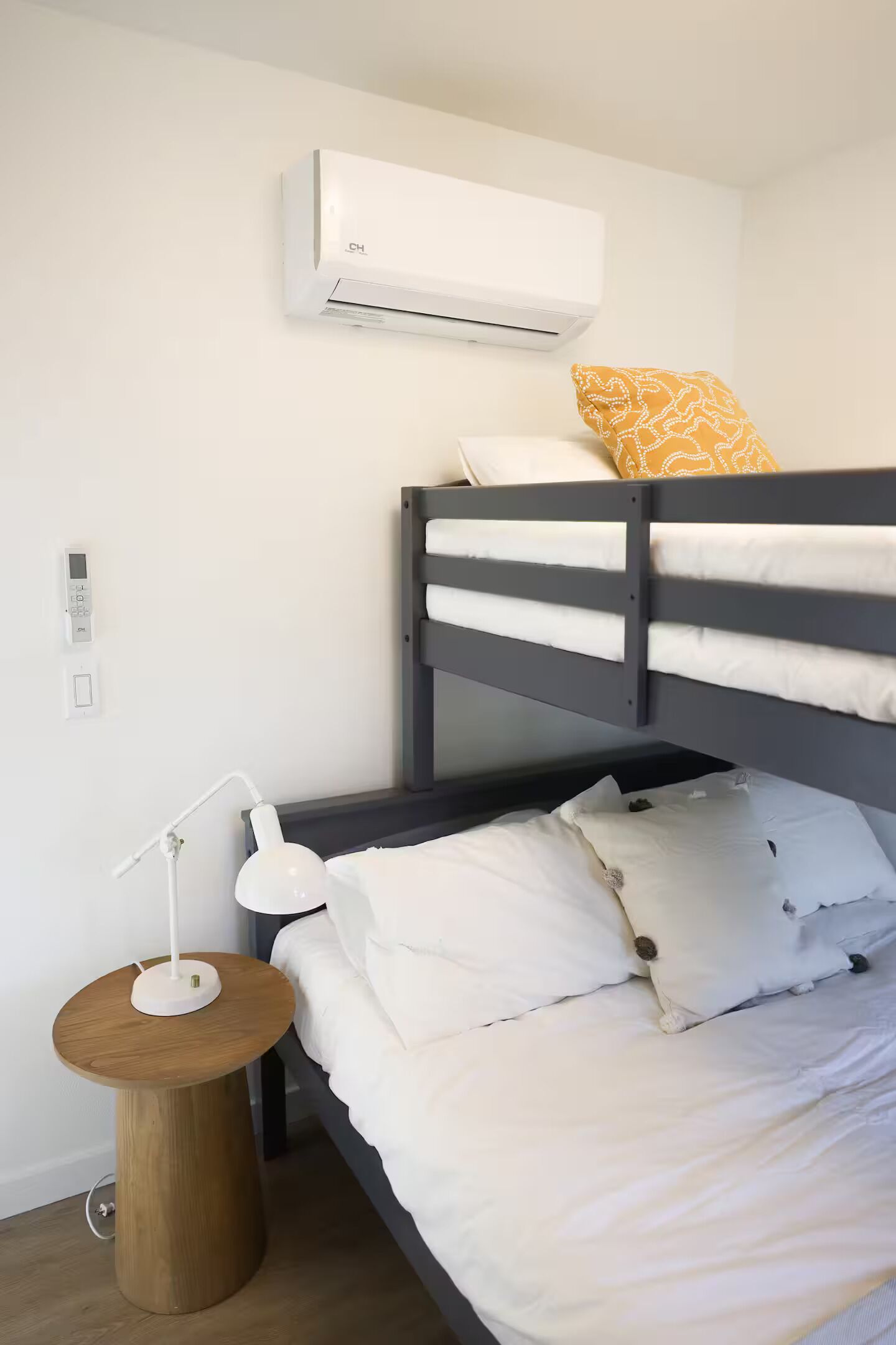 Ein Etagenbett mit weißer Bettwäsche, eine Nachttischlampe, ein kleiner Holztisch und eine Wand-Klimaanlage.