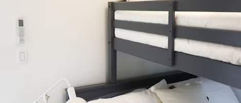Ein Etagenbett mit weißer Bettwäsche, eine Nachttischlampe, ein kleiner Holztisch und eine Wand-Klimaanlage.