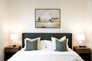 Een hotelkamer met een bed, twee nachtkastjes, een lamp en een schilderij aan de muur.