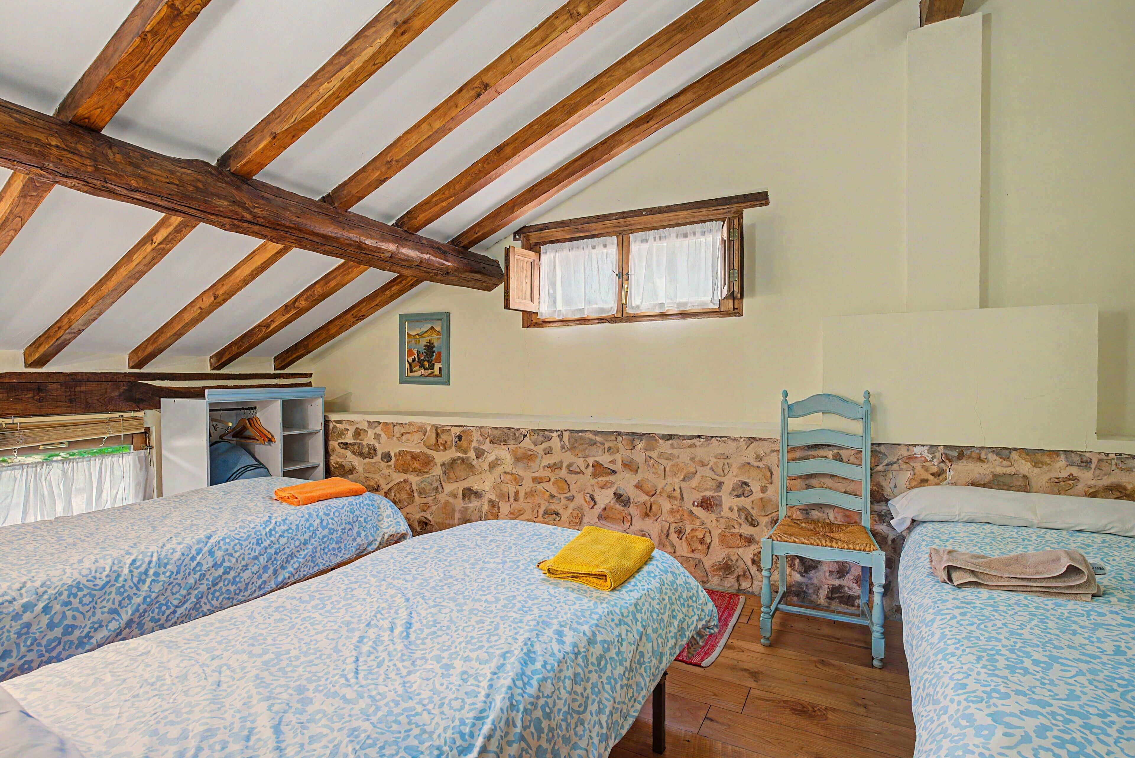 A bedroom with two beds, a wooden ceiling, a stone wall, and a small window.