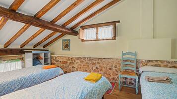 A bedroom with two beds, a wooden ceiling, a stone wall, and a small window.