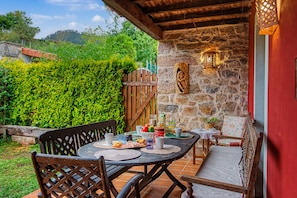 An outdoor dining area with a stone wall, wooden furniture, and a view of a lush garden.
