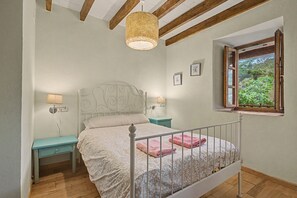 Un dormitorio con cama, mesitas de noche, una ventana con vistas y un techo con vigas a la vista.