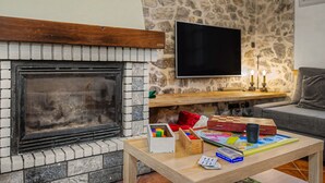 Ein Wohnzimmer mit Steinwand, Kamin, Flachbildfernseher und Couchtisch mit Gesellschaftsspielen.