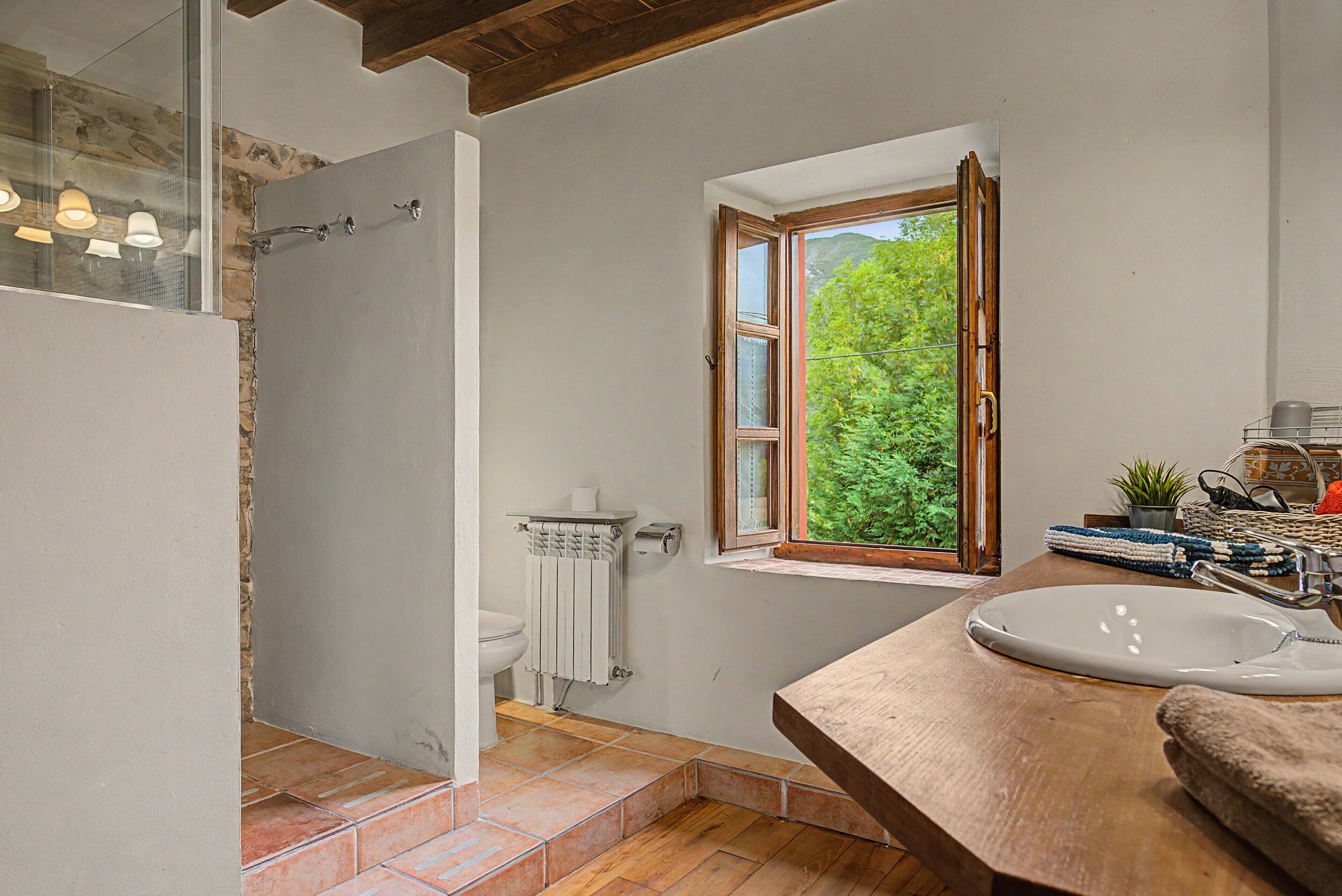 A bathroom with a shower, toilet, window, sink, and wooden floor.
