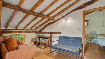 A rustic attic room with exposed wooden beams, a blue cushioned bench, a wooden table, and a sofa.