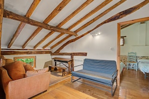 A rustic attic room with exposed wooden beams, a blue cushioned bench, a wooden table, and a sofa.