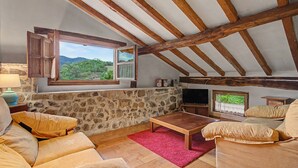 Ein rustikaler Raum mit einer Steinwand, Holzbalken, einem Holztisch und einer Couch.