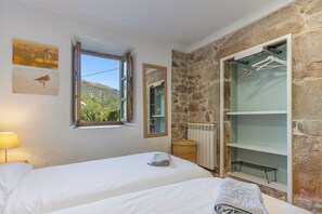 Un dormitorio con cama, ventana con vista a un bosque, pared de piedra y armario con perchas.