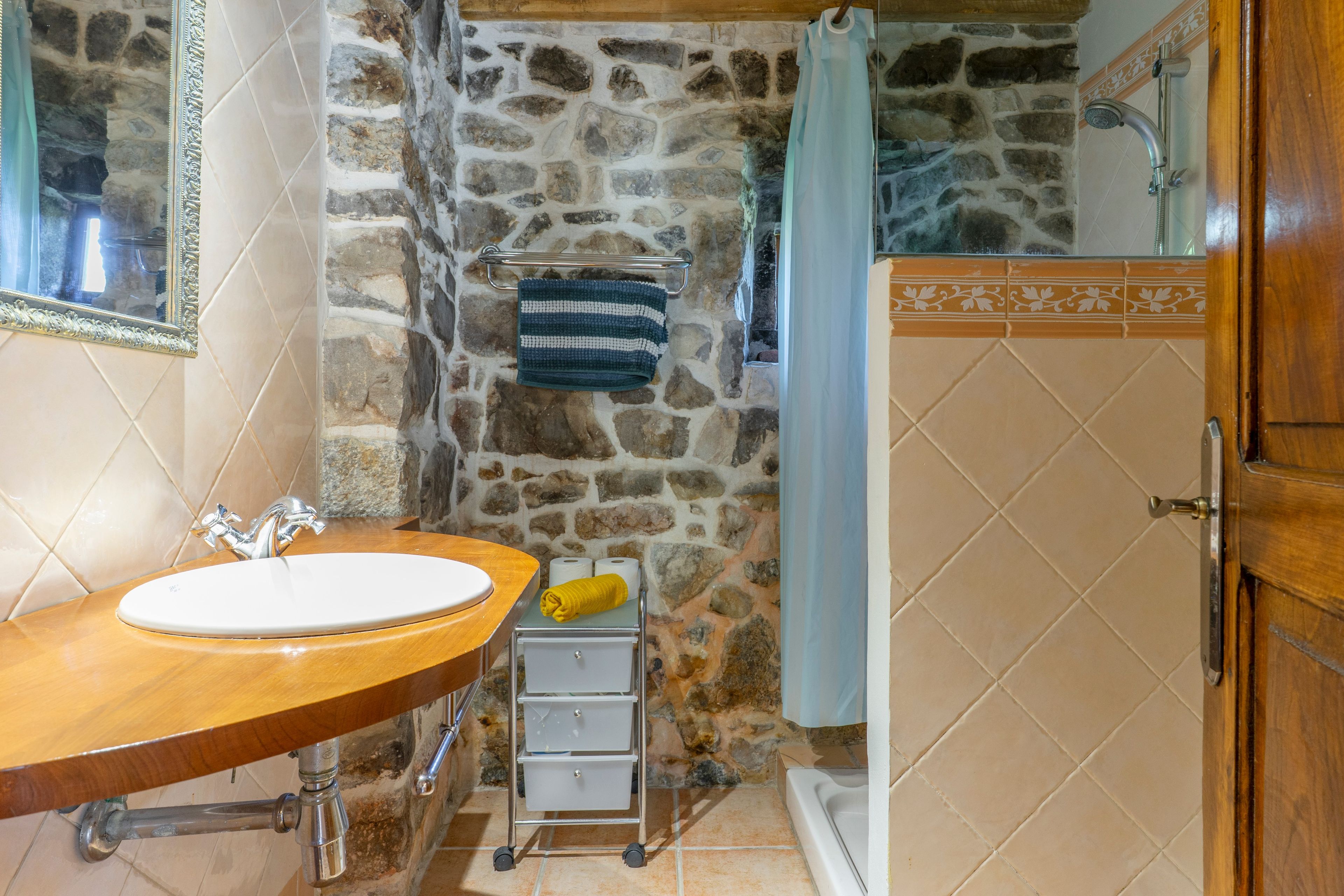 Un baño con pared de piedra, lavamanos de madera, bañera y un perchero para toallas.
