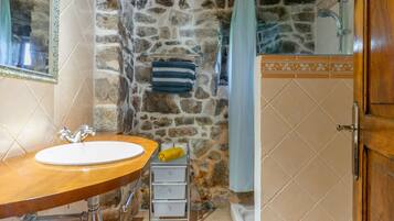 Un baño con pared de piedra, lavamanos de madera, bañera y un perchero para toallas.
