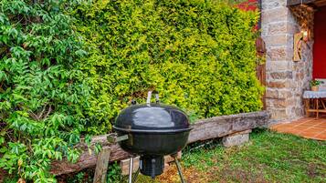 Una parrilla negra con tapa, ubicada en un área cubierta de césped con un muro de piedra y un seto al fondo.