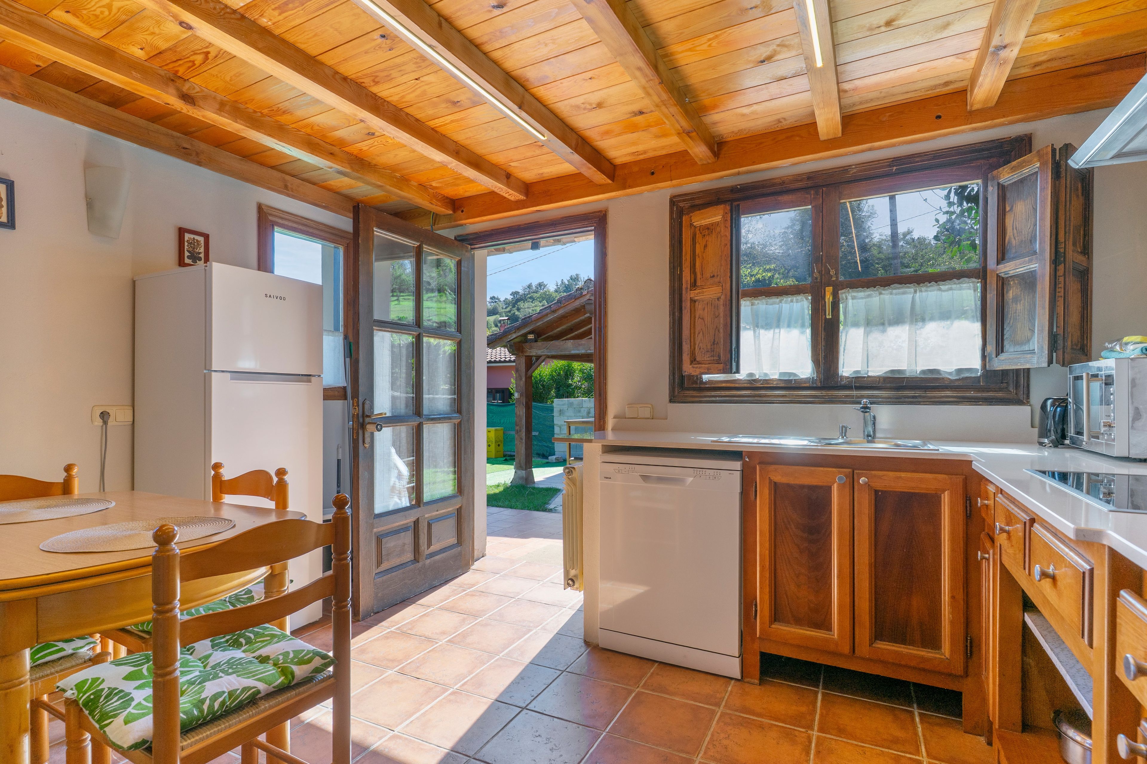 Una cocina con armarios de madera, lavavajillas y ventana con vistas a un jardín.