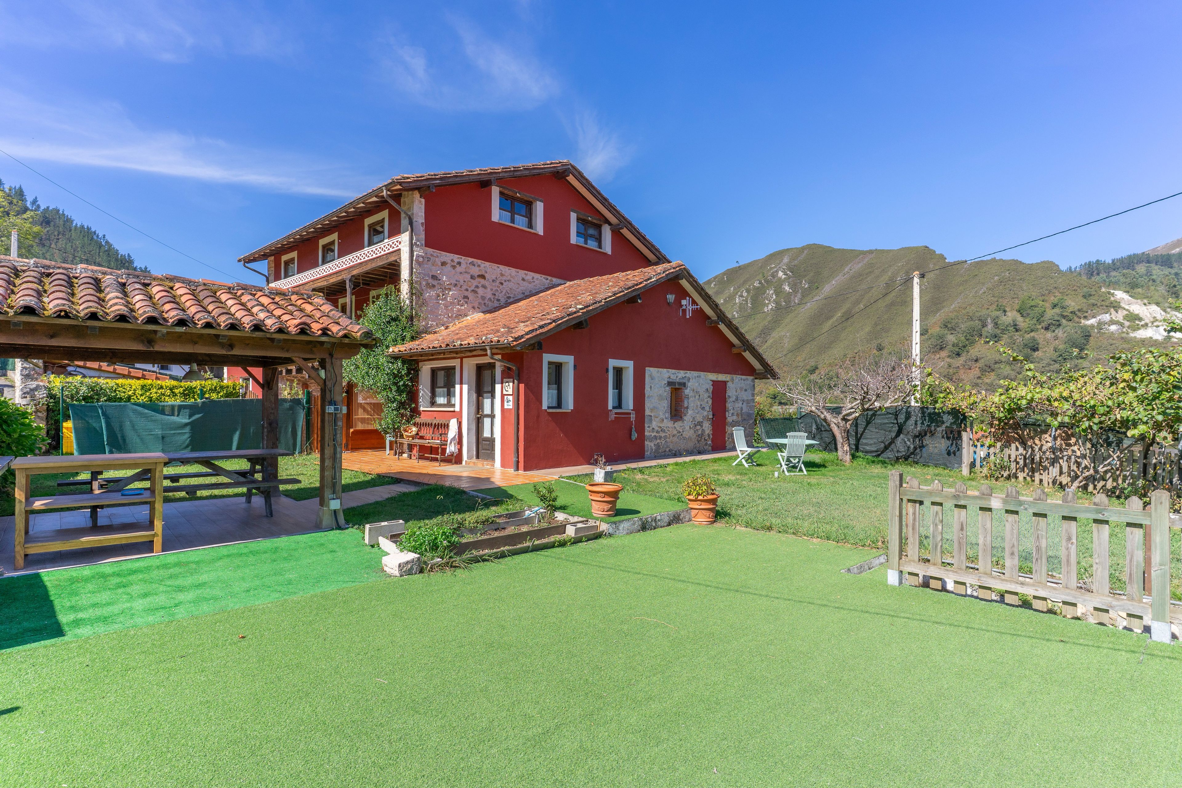 Una casa roja de dos pisos con techo de tejas, terraza de madera y césped cuidado.